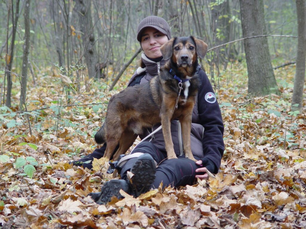 Ramona sitzt am Boden un dHund Chucky steht mit den Vorderbeinen auf Ramonas Bein. Beide schauen in die Kamera